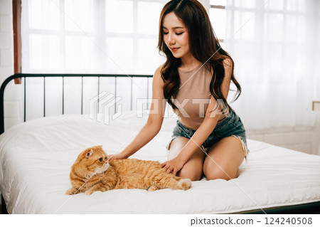 A heartwarming scene unfolds in a room as a woman lovingly strokes her orange Scottish Fold cat resting on the bed. Their connection radiates joy, happiness, and togetherness. Pat love A heartwarming scene unfolds in a room as a woman lovingly strokes her orange Scottish Fold cat resting on the bed. Their connection radiates joy, happiness, and togetherness. Pat love 124240508