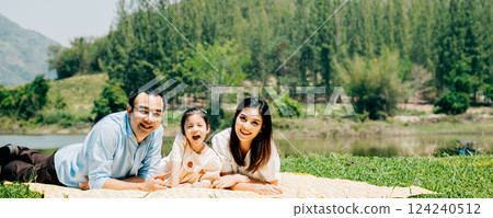 Asian family father mother and daughter lying on blanket spring meadow field grass in park cheerful sweet kid girl, parents and child picnic enjoying outdoors together, Family relaxation concept 124240512