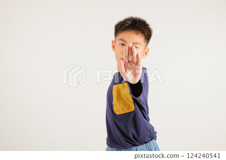 Asian portrait cute young kid boy smiling doing show stop sign gesture with palm of hand but unhappy face studio shot isolated on white background, primary children doubt with copy space 124240541