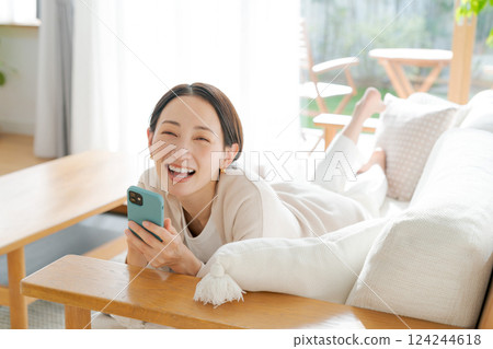 一位女士躺在沙發上看著她的智慧型手機 124244618