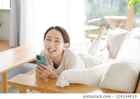 A woman lying on a sofa and looking at her smartphone A woman lying on a sofa and looking at her smartphone 124244619