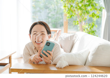 A woman lying on a sofa and looking at her smartphone 124244620