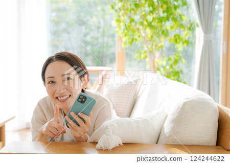 A woman lying on a sofa and looking at her smartphone 124244622
