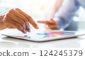 A close-up of a hand interacting with a tablet screen displaying a colorful pie chart. 124245379