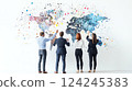 Four people dressed in business attire stand with their backs to the camera, pointing at a world map on a white wall 124245383