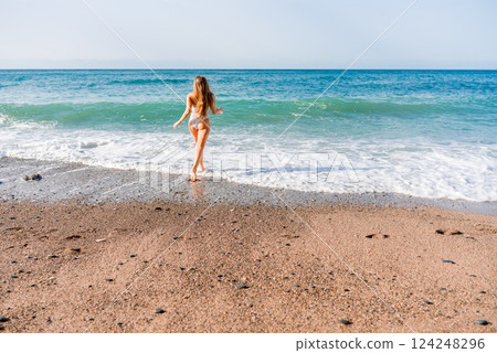 Happy woman in bikini running on the beach. Active leisure, a beautiful girl in a bikini is having fun on the beach, big waves are splashing along the beach. Happy woman in bikini running on the beach. Active leisure, a beautiful girl in a bikini is having fun on the beach, big waves are splashing along the beach. 124248296