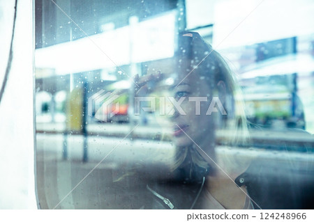 Woman traveler contemplating outdoor view from window of train. Young lady on commute travel to work sitting in bus or train Woman traveler contemplating outdoor view from window of train. Young lady on commute travel to work sitting in bus or train 124248966