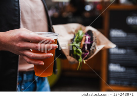 Close up of woman hands holding delicious organic salmon vegetarian burger and homebrewed IPA beer on open air beer an burger urban street food festival in Ljubljana, Slovenia 124248971