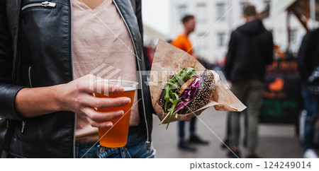 Close up of woman hands holding delicious organic salmon vegetarian burger and homebrewed IPA beer on open air beer an burger urban street food festival in Ljubljana, Slovenia 124249014