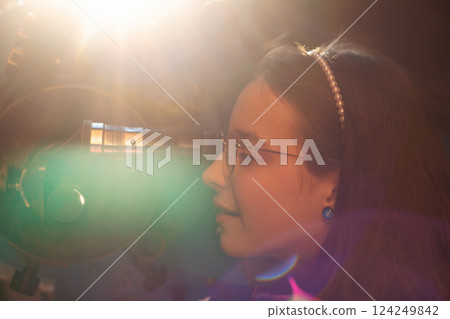 Young girl observes through telescope with sunlight flare. Young girl observes through telescope with sunlight flare. 124249842