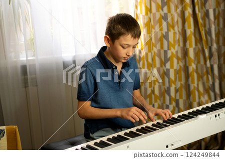 Boy in blue shirt playing digital piano near window Boy in blue shirt playing digital piano near window 124249844
