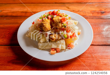Traditional chicharron dish with cassava and tomato salad. Latin food chicharron con yuca served on wooden table. Nicaraguan dish chicharron with cassava on the table. Traditional chicharron dish with cassava and tomato salad. Latin food chicharron con yuca served on wooden table. Nicaraguan dish chicharron with cassava on the table. 124254056