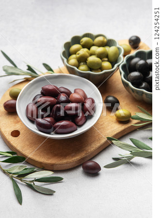 Kalamata, green and black olives displayed on wooden cutting board with olive branches Kalamata, green and black olives displayed on wooden cutting board with olive branches 124254251