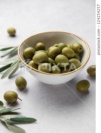 Fresh green olives in a bowl with olive branches on marble table Fresh green olives in a bowl with olive branches on marble table 124254257