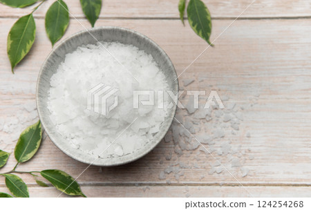 Magnesium flakes in bowl on wooden table with green leaves promoting relaxation and wellness 124254268