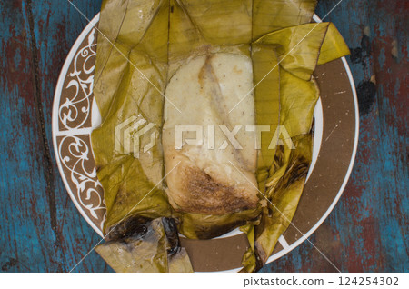 Traditional Tamal Pisque stuffed in banana leaf served on wooden table, Central American typical food Tamal Pisque stuffed. Stuffed tamale served on wooden table 124254302