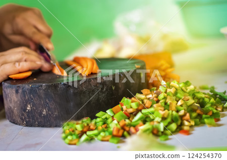 Hands cutting carrot pieces on a homemade chopper. Close up of hands chopping carrots in a wooden chopper. Concept of hands cutting vegetables in a wooden chopper 124254370