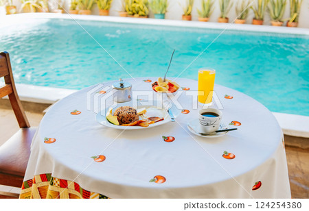 Traditional breakfast served at the table near a swimming pool. Breakfast served on the table with a swimming pool in the background. fruit salad Traditional breakfast served at the table near a swimming pool. Breakfast served on the table with a swimming pool in the background. fruit salad 124254380