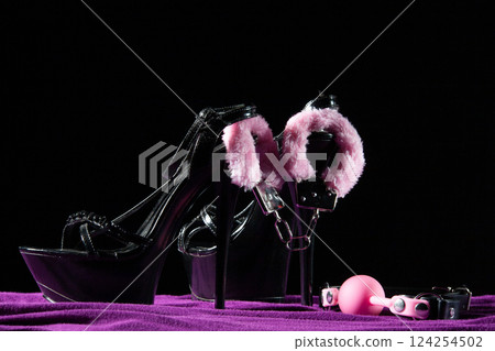 Adult sex games. Kinky lifestyle. Pink gag ball, handcuffs and a pair of black high-heeled shoes on the purple bedsheet. Bdsm outfit 124254502