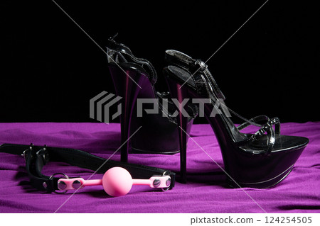 Adult sex games. Kinky lifestyle. Pink gag ball and a pair of black high-heeled shoes on the purple bedsheet. Bdsm outfit Adult sex games. Kinky lifestyle. Pink gag ball and a pair of black high-heeled shoes on the purple bedsheet. Bdsm outfit 124254505