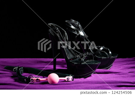 Adult sex games. Kinky lifestyle. Pink gag ball and a pair of black high-heeled shoes on the purple bedsheet. Bdsm outfit Adult sex games. Kinky lifestyle. Pink gag ball and a pair of black high-heeled shoes on the purple bedsheet. Bdsm outfit 124254506