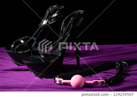 Adult sex games. Kinky lifestyle. Pink gag ball and a pair of black high-heeled shoes on the purple bedsheet. Bdsm outfit Adult sex games. Kinky lifestyle. Pink gag ball and a pair of black high-heeled shoes on the purple bedsheet. Bdsm outfit 124254507