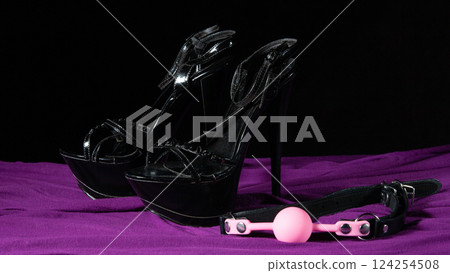 Adult sex games. Kinky lifestyle. Pink gag ball and a pair of black high-heeled shoes on the purple bedsheet. Bdsm outfit 124254508