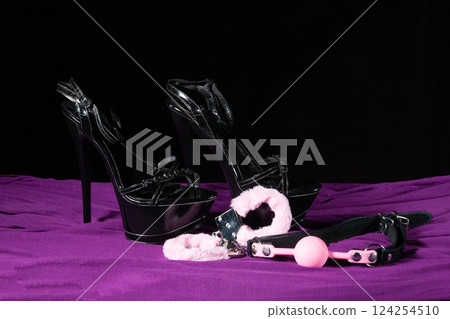 Adult sex games. Kinky lifestyle. Pink gag ball, handcuffs and a pair of black high-heeled shoes on the purple bedsheet. Bdsm outfit Adult sex games. Kinky lifestyle. Pink gag ball, handcuffs and a pair of black high-heeled shoes on the purple bedsheet. Bdsm outfit 124254510