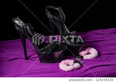 Adult sex games. Kinky lifestyle. Handcuffs and a pair of black high-heeled shoes on the purple bedsheet. Bdsm outfit Adult sex games. Kinky lifestyle. Handcuffs and a pair of black high-heeled shoes on the purple bedsheet. Bdsm outfit 124254516