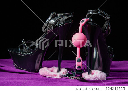 Adult sex games. Kinky lifestyle. Pink gag ball, handcuffs and a pair of black high-heeled shoes on the purple bedsheet. Bdsm outfit 124254525