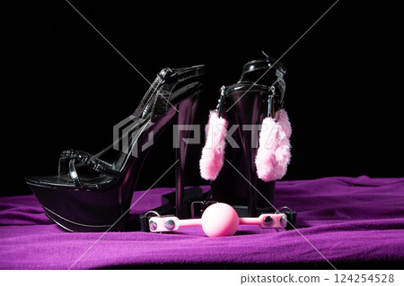 Adult sex games. Kinky lifestyle. Pink gag ball, handcuffs and a pair of black high-heeled shoes on the purple bedsheet. Bdsm outfit 124254528