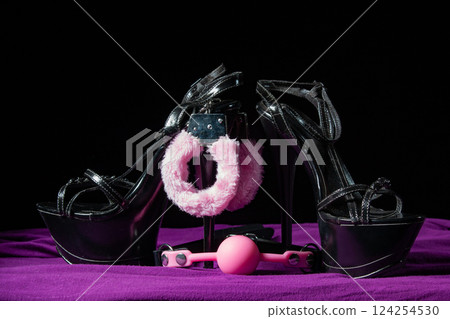 Adult sex games. Kinky lifestyle. Pink gag ball, handcuffs and a pair of black high-heeled shoes on the purple bedsheet. Bdsm outfit Adult sex games. Kinky lifestyle. Pink gag ball, handcuffs and a pair of black high-heeled shoes on the purple bedsheet. Bdsm outfit 124254530