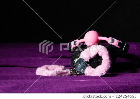 Bdsm outfit. Bondage handcuffs and Gag ball on the purple bedsheet. Adult sex games. Kinky lifestyle. Bdsm outfit. Bondage handcuffs and Gag ball on the purple bedsheet. Adult sex games. Kinky lifestyle. 124254555