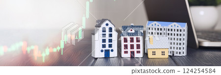 Miniature houses with stock market chart and laptop, symbolizing real estate investment, property market trends, and financial growth opportunities. 124254584