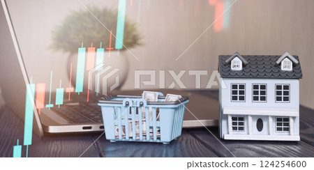 Workspace for online real estate shopping and market analysis with candlestick chart on laptop, miniature house, shopping cart with cash 124254600