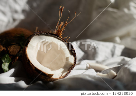 Fresh coconuts on a white cloth with one halved coconut revealing its inner flesh 124258030