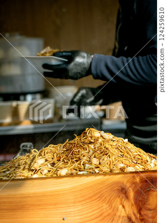 Street food festival in Europe. Asian fast food at market stall. Pile of stir-fried chicken noodles on tray, vendors gloved hands serving. Freshly made, vibrant, authentic flavors, quick meal. 124259610