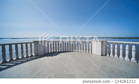 Marble terrace with ornate balusters framing serene lake waters, reflecting cloudless sky and radiating tranquil landscape atmosphere in Khabarovsk. Marble terrace with ornate balusters framing serene lake waters, reflecting cloudless sky and radiating tranquil landscape atmosphere in Khabarovsk. 124261212