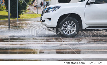 White sport utility vehicle driving fast on wet city street after rain, creating big splash of water White sport utility vehicle driving fast on wet city street after rain, creating big splash of water 124261249