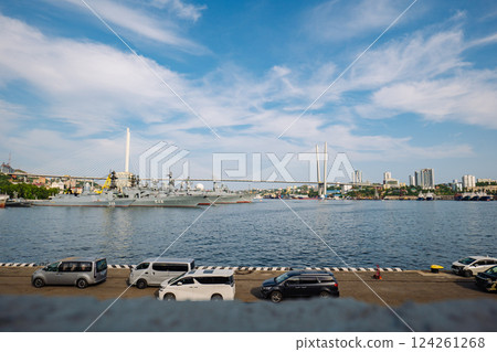 Russian naval vessels moored at vladivostok harbor, golden suspension bridge spanning scenic maritime backdrop under bright sunlight 124261268