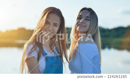 Two beautiful young school girlfriends are smiling and enjoying a relaxing sunset at the lake Two beautiful young school girlfriends are smiling and enjoying a relaxing sunset at the lake 124261285