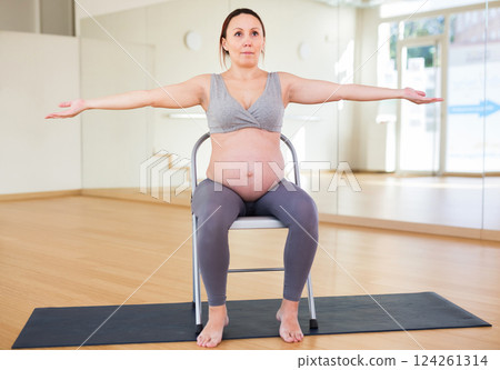 Pregnant woman is engaged in yoga. Exercise on chair with arms spread apart Pregnant woman is engaged in yoga. Exercise on chair with arms spread apart 124261314