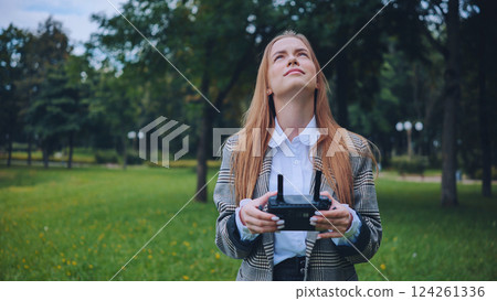 Businesswoman piloting a drone in a park, enjoying modern technology and outdoor activities 124261336
