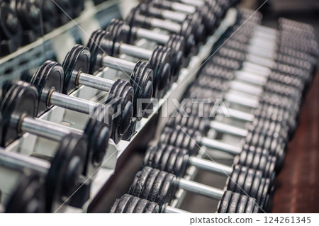Many dumbbells are neatly arranged in rows on a rack, ready for a workout session in the gym 124261345