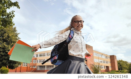 Schoolgirl running near campus, carrying notebooks, wearing backpack and glasses, embracing academic excitement Schoolgirl running near campus, carrying notebooks, wearing backpack and glasses, embracing academic excitement 124261348