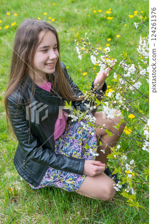 Teenage girl wearing floral skirt and leather jacket standing amid yellow dandelions, enjoying blossoming wildflower meadow 124261376