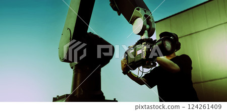 Video or film production with high tech robotic arm equipped with a professional cinema camera. Operated by a cinematographer. Advanced motion control system enables precise camera movements filming. 124261409