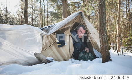 Alcohol addicted homeless man seeks refuge from the cold in a makeshift tent in a snowy forest during the winter Alcohol addicted homeless man seeks refuge from the cold in a makeshift tent in a snowy forest during the winter 124261439