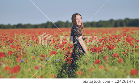 Young woman smiling, standing amid blooming red poppies, basking in warm summer sunlight Young woman smiling, standing amid blooming red poppies, basking in warm summer sunlight 124261472