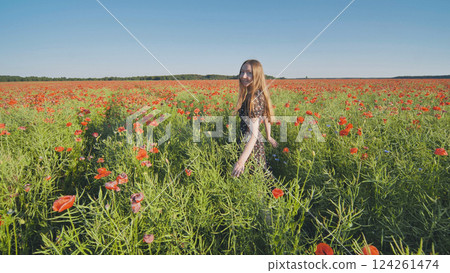 Joyful female wandering through vibrant poppy meadow, gently caressing crimson blooms under warm sunlight 124261474
